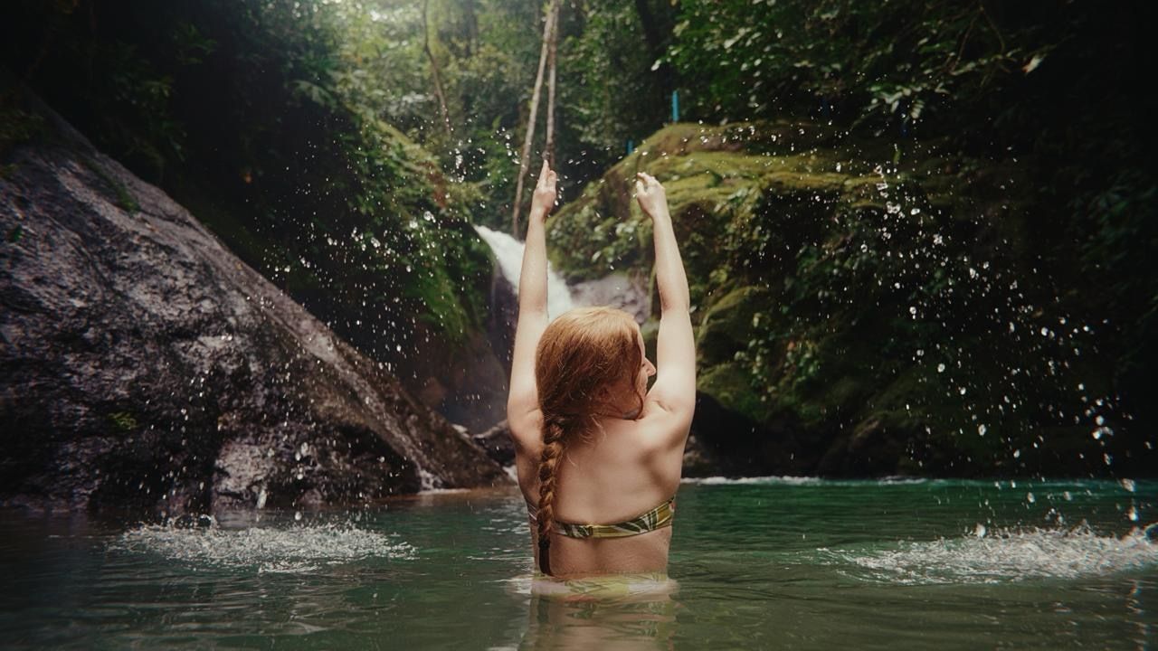 A woman splashing water at a jungle waterfall
