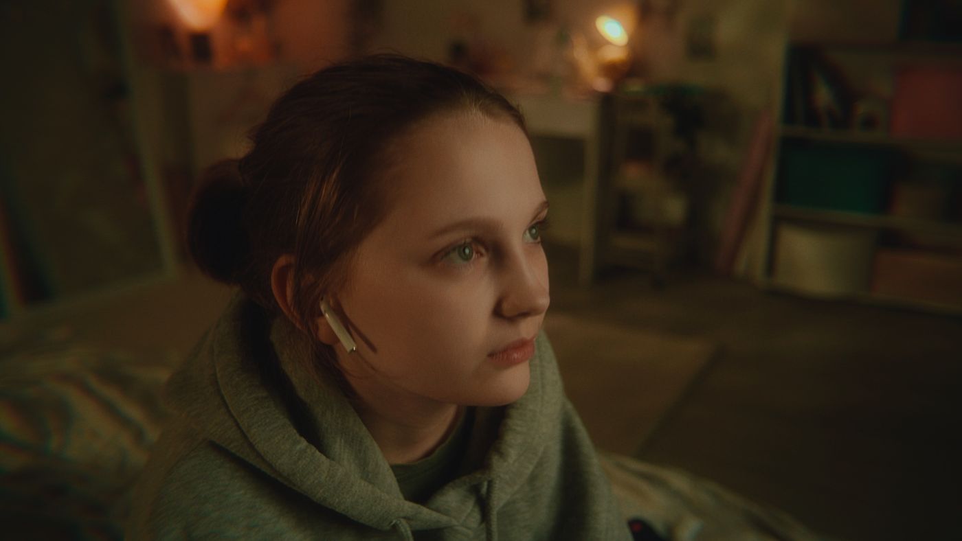 A girl lit by a practical lamp in a dim bedroom