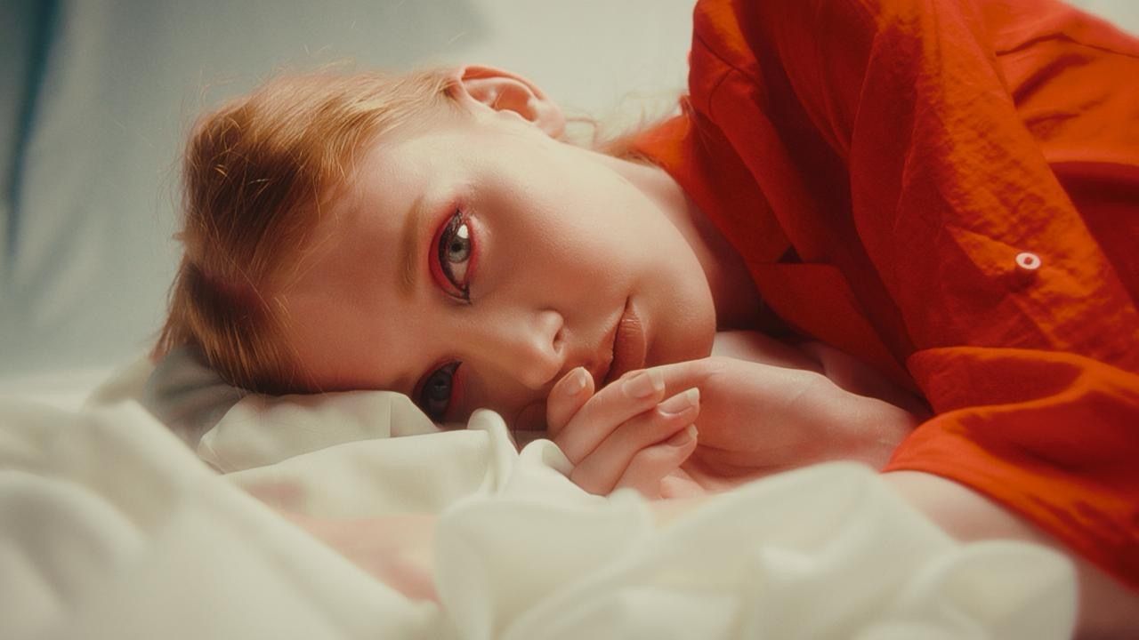 A red-haired woman lying in white sheets, with film grain