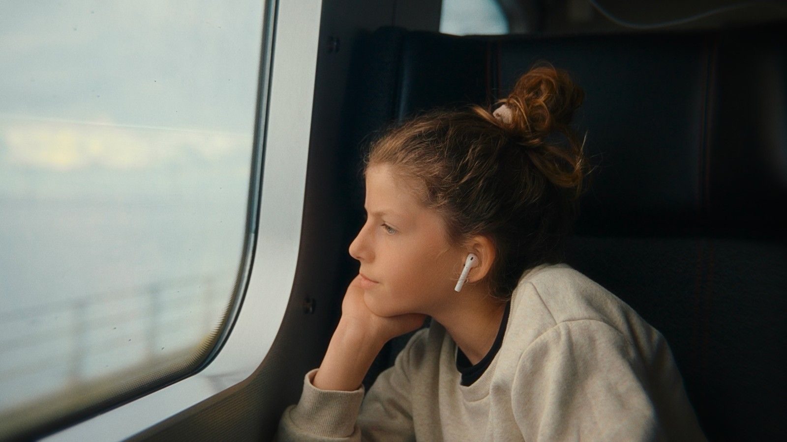A girl on a train looking out an overcast window, graded on film